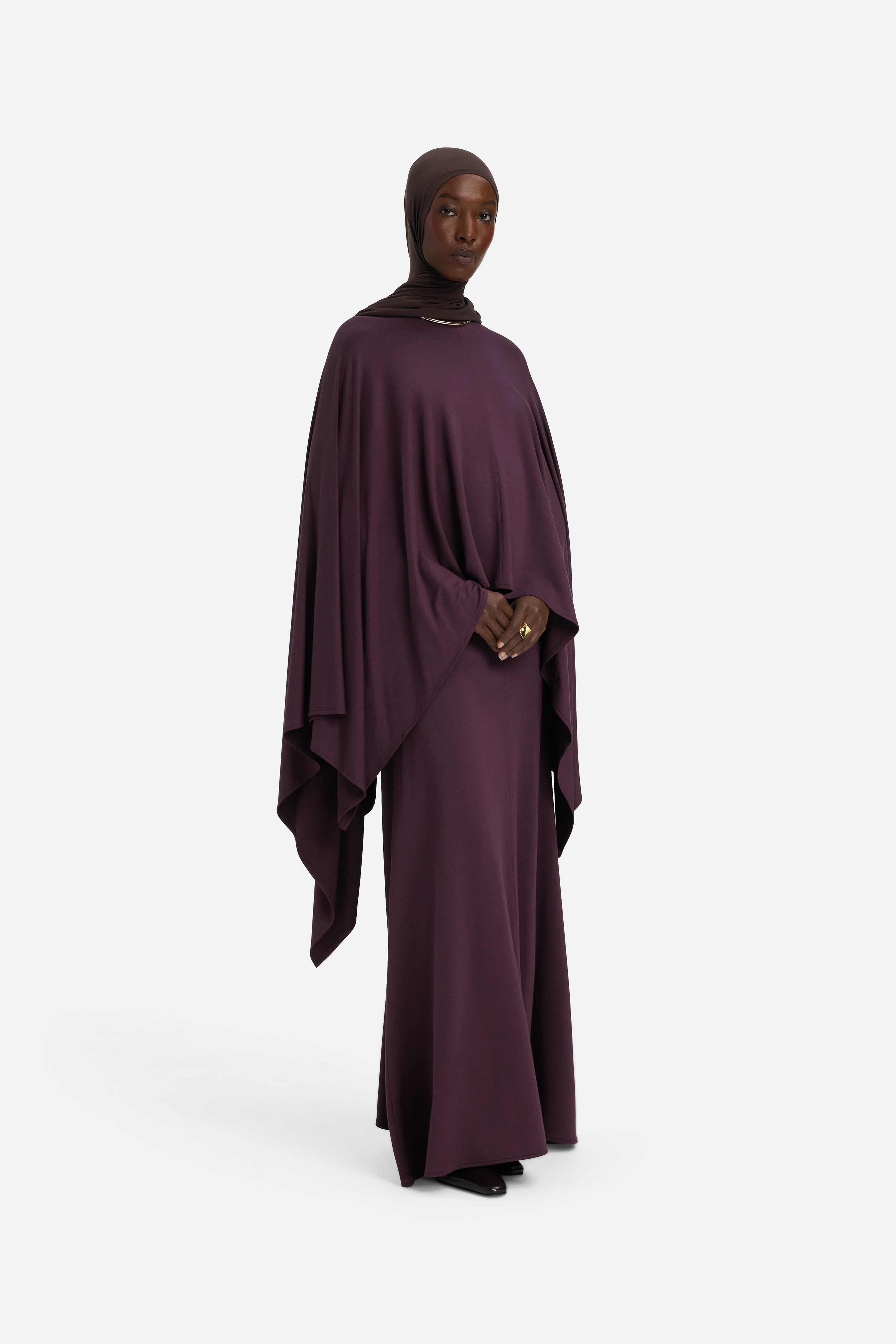 Model wearing purple cape and brown headscarf, side view