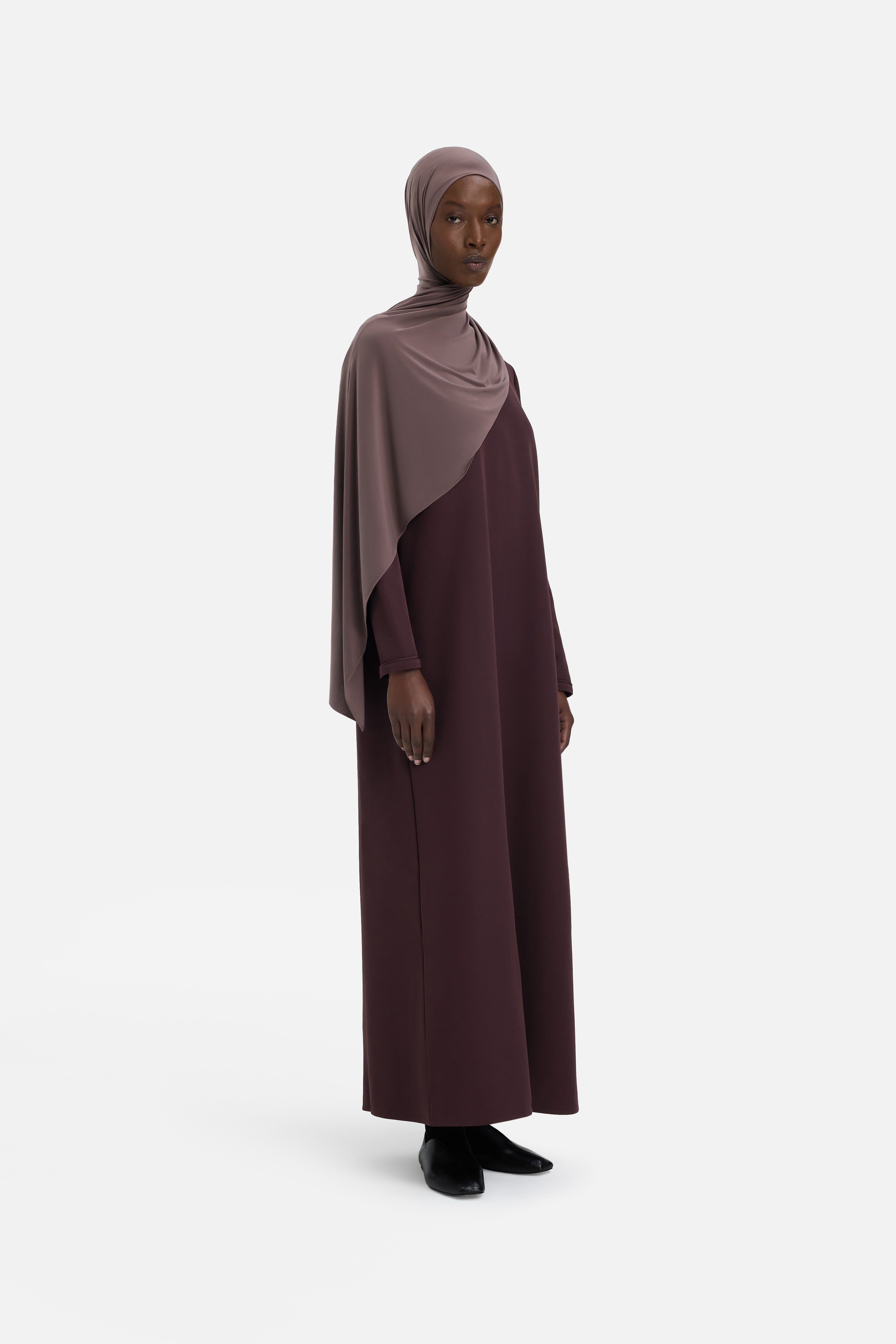 Model wearing purple dress and headscarf, side view