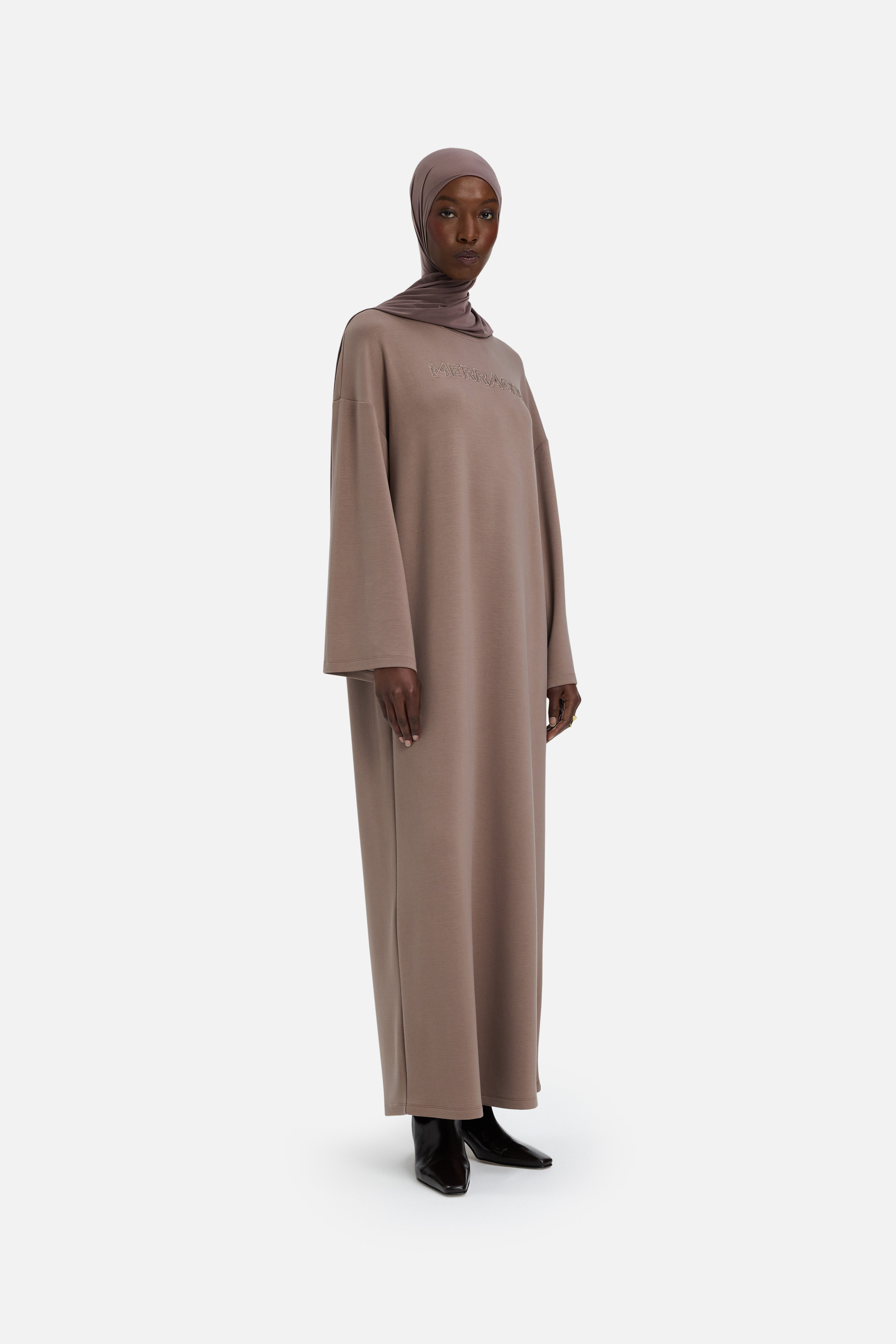 Model wearing modest taupe dress and headscarf, side view
